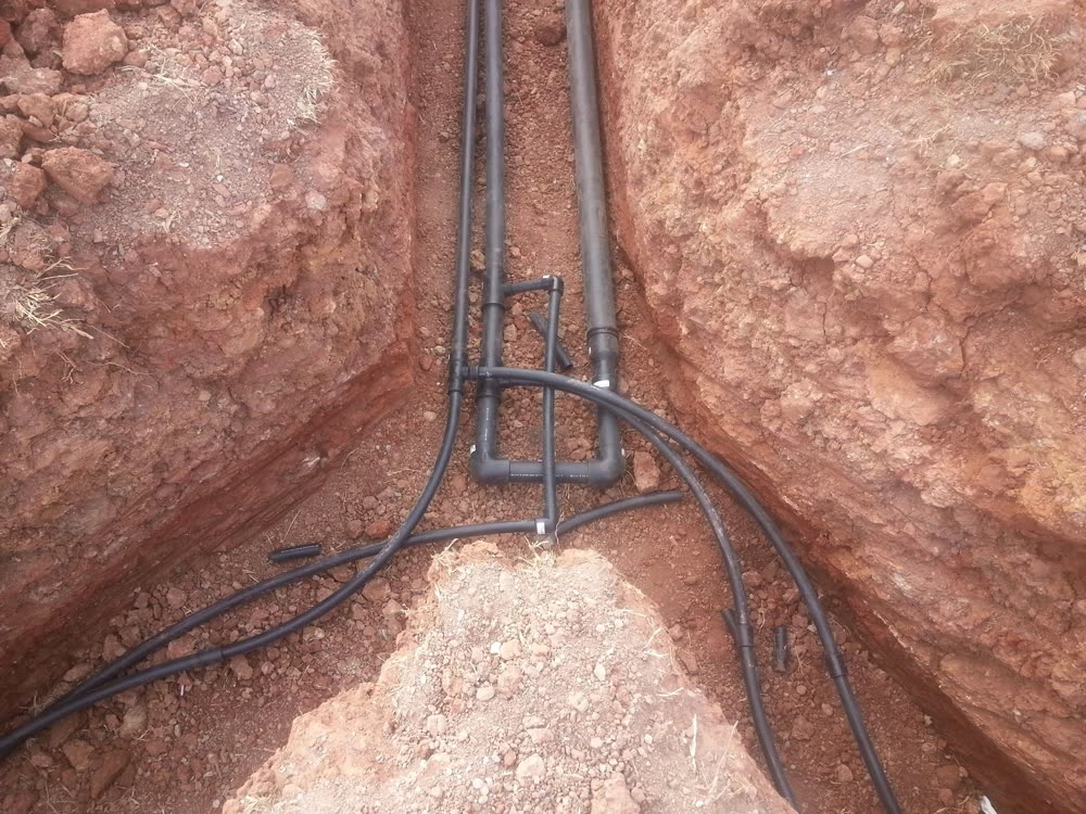 A trench in red clay with geothermal loop pipes laid in it